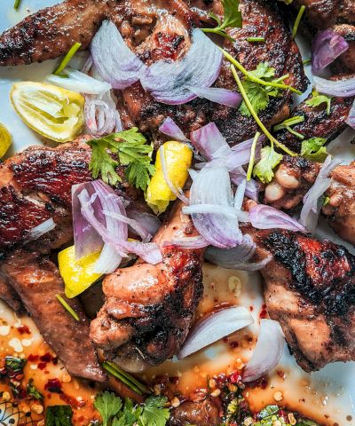 Grilled meat pieces topped with lemon wedges, sliced red onions, herbs, and spices in a savory sauce, ready to eat.
